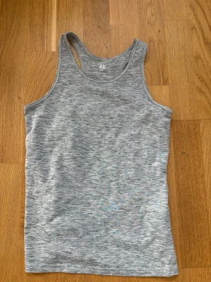 Grå sportig linnetopp från H&M - Snygg gråmelerad linnetopp från H&M Sport. Modellen är ärmlös med klassisk racerback och tillverkad i ett mjukt och stretchigt syntetmaterial som passar perfekt till träning eller chill. Enkel och stilren design som är lätt att matcha.