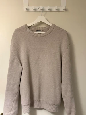 Beige stickad tröja från Weekday - Säljer en stilren beige stickad tröja från Weekday. Tröjan har rund halsringning, långa ärmar och ribbade muddar vid ärmslut och nederkant. Perfekt för lager på lager och enkel att matcha med olika outfits.