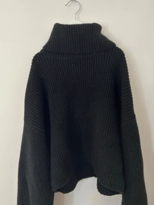 Svart tröja med krage från Monki - Säljer en svart stickad polotröja från Monki i storlek XS. Tröjan har en hög, ribbad polokrage och breda ärmar med avslappnad passform. Perfekt för kyliga dagar och enkel att styla till olika outfits.