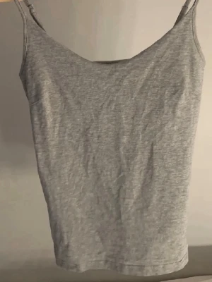 Grå  linne - Snygg grå linne med smala axelband. Perfekt att styla till jeans eller kjol för en enkel och clean look. Mjuk och stretchig känsla som sitter skönt på kroppen.