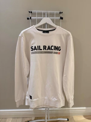 Vit sweatshirt från Sail Racing - Vit sweatshirt från Sail Racing med tryck framtill i svart och grått. Helt oanvänd 