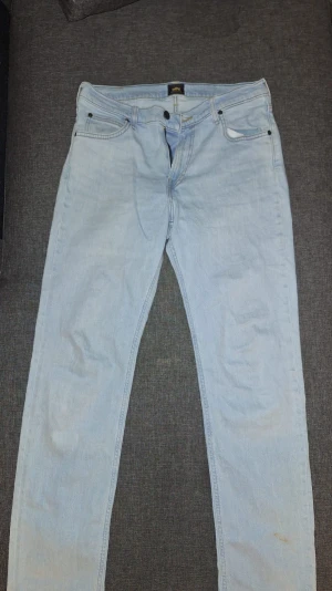 Ljusblå jeans från Lee - Säljer ett par ljusblå jeans från Lee med klassisk femficksmodell och raka ben. Jeansen har Lee-lapp bak i midjan och är tillverkade i bomull. Perfekta för en avslappnad och trendig look.
