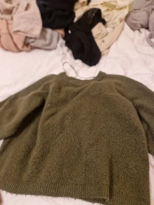 Olivgrön stickad tröja 157 XS - Mysig olivgrön stickad tröja från 157 i storlek XS. Tröjan har en enkel, rak passform med rund halsringning och ribbade muddar vid ärmslut och nederkant. Perfekt för lager på lager och chill dagar.
