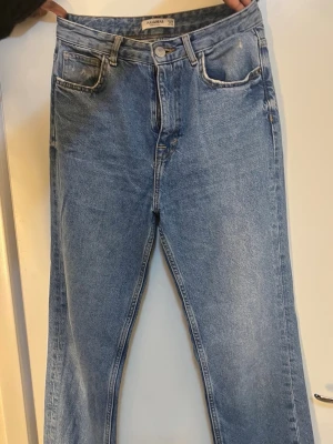 Blå raka jeans från Allsaints - Klassiska blå jeans från Allsaints med rak passform och hög midja. Jeansen har fem fickor, bälteshällor och stängs med knapp och dragkedja. Tillverkade i ett slitstarkt denimtyg som ger en tidlös look. Slits vid benet 