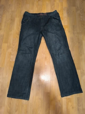 Mörkblå jeans med raka ben - Säljer ett par mörkblå jeans med raka ben och klassisk femficksdesign. Jeansen har normal midja och subtila sömmar på bakfickorna. Materialet är denim i bomull och passformen är avslappnad. Perfekta för en chill och stilren look.