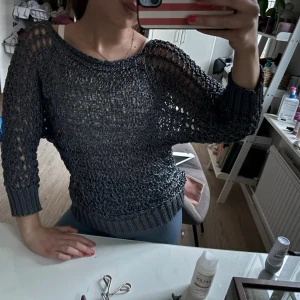 Mörkgrå stickad meshtröja - Snygg mörkgrå stickad meshtröja med lång ärm och bred ribbad mudd vid ärmslut och nederkant. Tröjan har en luftig, genombruten stickning som ger en cool och avslappnad vibe. Perfekt att styla lager på lager.