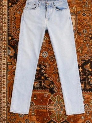 Ljusblå raka jeans från Nudie - Säljer ett par ljusblå raka jeans från Nudie Jeans med klassisk femficksmodell och subtila vågdetaljer på bakfickorna. Jeansen har normal midja och är tillverkade i mjuk denim, perfekta för en avslappnad och trendig look. 30/32 storlek. Väldigt bra skick, har dock lyckats få bort de flesta väck på bilderna, är egentligen några få mer. Skriv om fler bilder eller pris! (Lyckades få första bilden mer ljusare än de andra, skulle mer säga att de andra är den mer äkta färgen på byxorna)