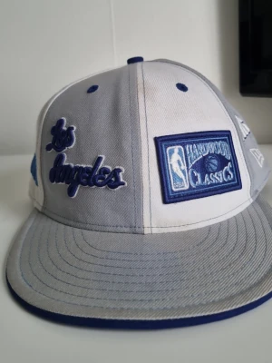 NBA Hardwood Classics Los Angeles keps - Snygg keps från New Era med broderad text 'Los Angeles' och NBA Hardwood Classics-logga. Kepsen är tvåfärgad i vitt och ljusblått och platt skärm. Perfekt för dig som gillar basket och streetwear. Kepsen är använd. Det är märkbart men det är inget fel på kepsen. Pris kan diskuteras. Fraktas inom 24 timmar.
