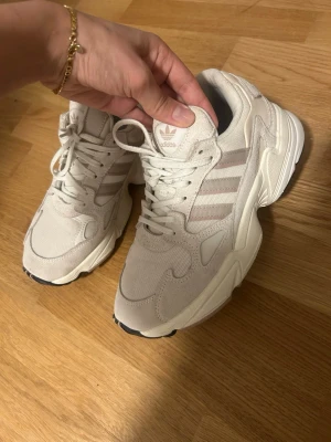 Beige Adidas sneakers med mesh och mocka - Säljer ett par snygga beige Adidas sneakers med klassiska tre ränder på sidan. Skorna har en chunky sula, ovandel i mesh och mocka samt snörning framtill. Perfekta för dig som gillar streetwear och vill ha en clean look.