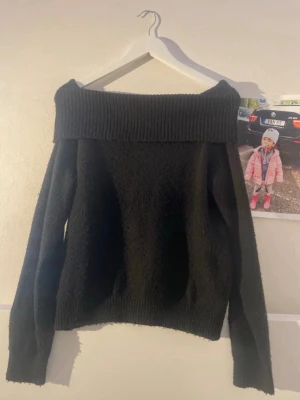 Svart off shoulder tröja - Säljer en svart off shoulder tröja med bred ribbstickad krage och långa ärmar. Tröjan har en mjuk och lite fluffig struktur, samt ribbade muddar vid ärmslut och nederkant. Perfekt för dig som gillar en trendig och avslappnad stil.