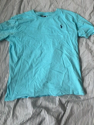 Turkos t-shirt från Ralph Lauren - Snygg turkos t-shirt från Ralph Lauren med klassisk rund hals och korta ärmar. T-shirten har den ikoniska lilla broderade loggan på bröstet och är gjord i mjuk bomull. Perfekt för en avslappnad och stilren look. Är storlek M men sitter som S