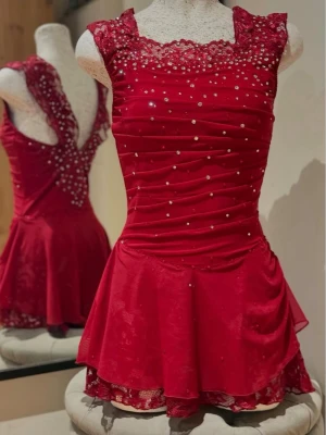 Röd paljettprydd maskeraddräkt - Snygg röd maskeraddräkt med glittrande paljetter och spetsdetaljer vid halsringningen. Klänningen har korta ärmar, markerad midja och ett utsvängande kjolparti i mesh. Perfekt för dans, show eller cosplay.