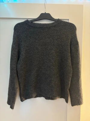 Mörkgrå stickad tröja - En enkel och stilren mörkgrå stickad tröja med rund halsringning och långa ärmar. Tröjan har råkat krympa när jag tvättat sen så den är kort i armarna men den är fortfarande jättefin 