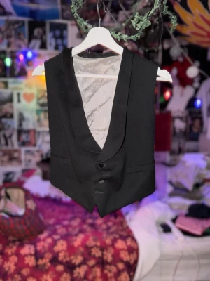 Svart kostymväst - kostymväst med klassisk sjalkrage och tre knappar framtill. Västen har två fickor och är fodrad med ljusgrått tyg på insidan. Perfekt att styla över en skjorta👔