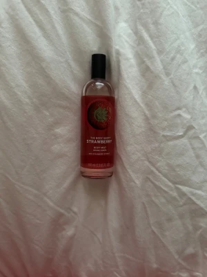 The Body Shop Strawberry Body Mist - Fräsch body mist från The Body Shop med doft av jordgubb. Kommer i en genomskinlig glasflaska med svart plastlock och röd etikett med jordgubbsbild. Innehåller 100 ml och har en söt, fruktig doft som känns ungdomlig och lätt.