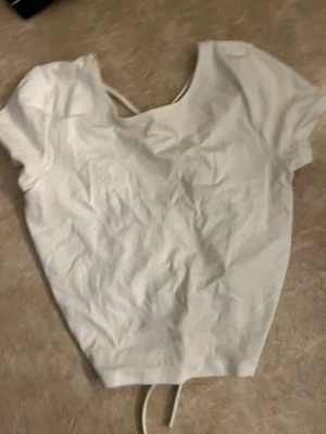 Vit croppad topp med snörning - Snygg vit croppad topp med korta ärmar och snörning i ryggen. Perfekt till höga jeans eller kjol. Enkel och stilren design som passar till många olika looks.