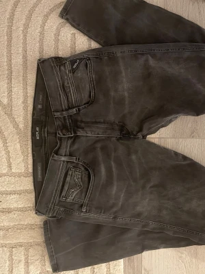 Svarta Replay jeans med tvättad look - Säljer ett par svarta jeans från Replay med snyggt tvättad finish och klassisk femficksdesign. Jeansen har raka ben och är tillverkade i bomull med stretch för extra komfort. Perfekt för dig som gillar en avslappnad och trendig stil.