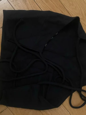 Svart snörad linnetopp - Snygg svart linnetopp med smala axelband och snörning i där bak med öppen rygg. Toppen har en enkel, croppad passform och är perfekt för att styla med jeans eller kjol. Materialet är av lite tjockare material men mjukt. 