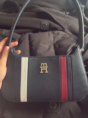 Klädpaket! Två hollies jackor + th väska - Snygg marinblå handväska från Tommy Hilfiger i läderimitation med vita och röda ränder framtill. Väskan har ett guldfärgat TH-emblem och ett kort axelband. Perfekt accessoar för en trendig look. Sen två fina svarta jackor en mest till vinter och andra till höst med kedja under!