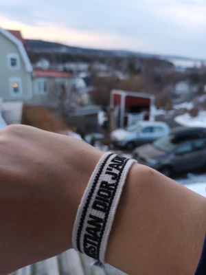 Christian Dior J'Adior tygarmband - Säljer ett snyggtChristian Dior med texten 'J'Adior' armband i vit med svart text. Armbandet har en enkel och trendig design med justerbar knytning. Perfekt accessoar för att lyfta din outfit med en exklusiv och grisch touch.
