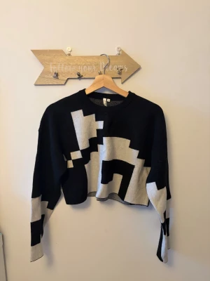Svart och vit cropped stickad tröja från Nelly - Svart stickad tröja från NLY Trend med vit pixelmönstrad design. Croppad modell med rund halsringning och långa ärmar. Perfekt för dig som gillar en edgy och modern stil.