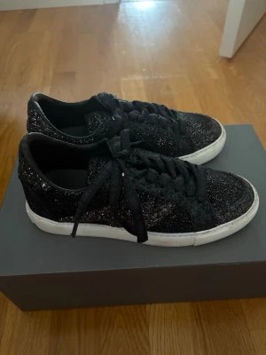 Svarta glittriga sneakers från Zadig & Voltaire - Snygga svarta sneakers från Zadig & Voltaire som är glittriga med vita sulor. Skorna har svarta skosnören och diskreta logodetaljer på tungan. De är använda ett fåtal gånger