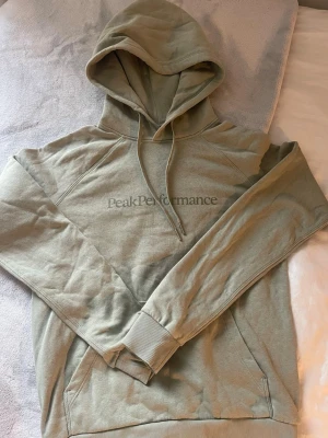 Grön hoodie från Peak Performance - Snygg grön hoodie från Peak Performance med klassisk logga på bröstet. Hoodien har huva med dragsko, ribbade muddar och en ficka. 