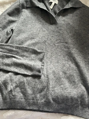 Grå stickad tröja med krage Arket - Snygg grå stickad tröja från Arket med klassisk krage och v-ringning. Tröjan har långa ärmar och ribbade muddar vid ärmslut och nederkant. Perfekt för lager på lager och enkel att matcha med olika stilar.
