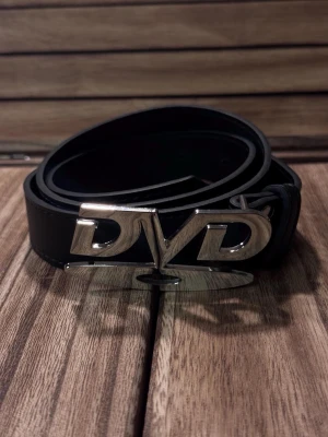 Svart Y2K bälte med DVD-spänne - Snyggt svart bälte med ett stort, blankt metallspänne i form av bokstäverna 'DVD'. Bra skick, 122 Cm lång