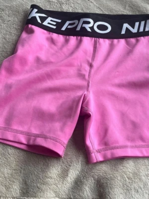 3 par Nike Pro shorts i rosa lila och blå - Tre par Nike Pro shorts i stretchigt funktionsmaterial, ett par i rosa, lila och ett par i ljusblått. Alla har bred svart resår med Nike Pro-logga och korta ben. Perfekta för träning eller gympass. Sitter som xs och xxs eftersom att de e barn