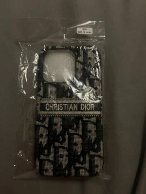 iPhone 14 Christian Dior mobilskal - Snyggt mobilskal med Christian Dior-logga och klassiskt svartvitt mönster. Skalet har en textil-liknande yta och är designat för att ge din mobil en exklusiv look. Passar perfekt för dig som gillar mode och vill sticka ut med din telefon.