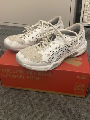 Vita Asics sneakers med meshdetaljer - Snygga vita sneakers från Asics med klassisk logga i svart på sidan. Skorna har meshpaneler för extra ventilation och vita snören. Yttermaterialet är en mix av syntet och textil vilket ger en sportig look. Perfekta för dig som gillar stilrena och bekväma sneakers.