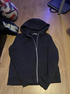 Svart zip hoodie med huva - En enkel svart hoodie med dragkedja framtill och justerbar huva. Hoodien har långa ärmar och ribbade muddar vid ärmslut och nederkant. Perfekt för en avslappnad och chill stil.