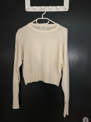 Vit stickad tröja från ONLY - Klassisk vit stickad tröja från ONLY med rund halsringning och långa ärmar. Tröjan har ribbade muddar vid ärmslut och nederkant samt en något croppad passform. Perfekt för lager på lager och enkel att matcha med olika stilar.