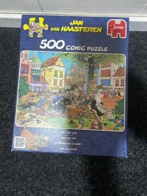 Jan van Haasteren 500-bitars pussel - Roligt och färgglatt 500-bitars pussel från Jan van Haasteren med ett komiskt stadsmotiv där folk jagar en katt. Pusslet kommer i originalkartong och har många detaljer i blått, grönt och rött. Perfekt för dig som gillar utmanande och humoristiska pussel.
