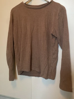 Beige/brun långärmad topp från H&M - En enkel och stilren brun långärmad topp från Uniqlo. Toppen har rund halsringning och är gjord i mjuk bomull, perfekt för en avslappnad look. Passformen är normal och färgen är diskret beige-brun.