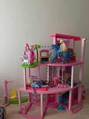 Barbiehus med dockor och tillbehör - Stort Barbiehus i rosa plast med tre våningar, möbler och flera Barbie-dockor. Inkluderar hästar, enhörningar, gungställning och olika smådjur. Huset har öppna ytor, detaljerade rum och färgglada accessoarer. Perfekt för fantasifull lek och samling.