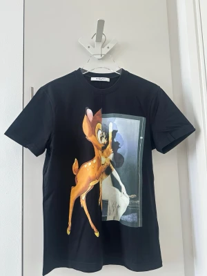Svart Givenchy t-shirt med Bambi-tryck - Svart t-shirt från Givenchy med ett stort färgglatt Bambi-tryck framtill. Klassisk rund halsringning och korta ärmar. Tillverkad i mjuk bomull för en skön känsla och snygg passform. Perfekt för dig som vill sticka ut med en ikonisk design.