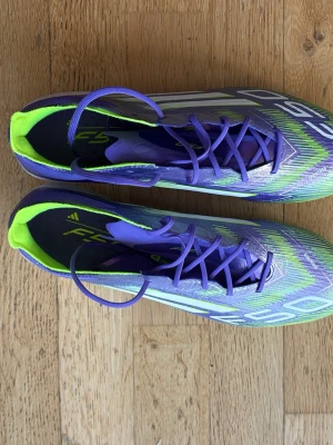 Adidas F50 lila och gröna fotbollsskor - Säljer ett par Adidas F50 fotbollsskor i en riktigt snygg lila och grön färgkombination med vita detaljer. Skorna har en låg profil, snörning och ovandel i syntetmaterial för lätt vikt och bra bollkontroll. Perfekta för dig som vill sticka ut på planen!.skorna är dessutom aldrig använda och priset kan diskuteras 