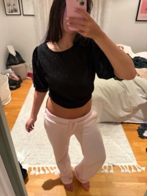 Svart glittrig croppad topp - Säljer en svart croppad topp med glittrigt tyg och puffiga korta ärmar. Toppen har en rund halsringning och sitter snyggt tight över kroppen. Perfekt för dig som vill ha något extra till outfiten!