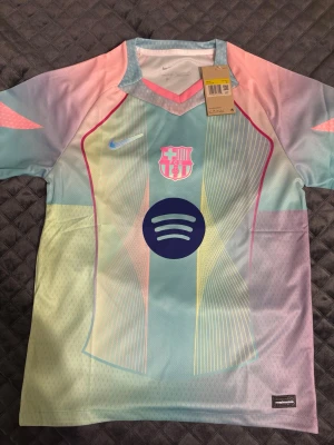Nike FC Barcelona pastell matchtröja - Säljer en FC Barcelona matchtröja från Nike i snygga pastellfärger med inslag av ljusblått, rosa och gult. Tröjan har klubbmärke, Nike-logga och Spotify som sponsor på bröstet. Tillverkad i Dri-FIT material som andas, perfekt för träning eller match.