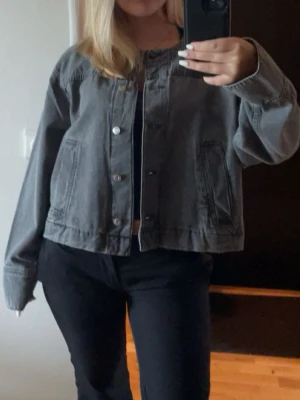 Grå jeansjacka - Säljer en grå jeansjacka med raka ärmar och silverfärgade knappar framtill. Jackan har två snedställda fickor och en klassisk, avslappnad passform. Perfekt att slänga över en hoodie eller t-shirt för en cool look.