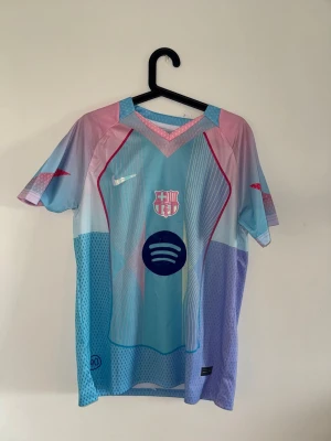 Barcelona Nike matchtröja blå/rosa - Säljer en Barcelona matchtröja från Nike i blått och rosa med klubbmärke och Spotify-logga på bröstet. Tröjan har korta ärmar, sportig passform och är tillverkad i ett lätt, ventilerande material perfekt för fotboll eller träning.
