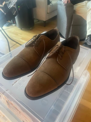 Bruna mockaloafers från Rossi - Helt nya bruna loafers i mocka med klassisk snörning och låg klack. 1800kr. Skorna har en stilren design med rundad tå och diskreta sömmar över tån. Perfekta för dig som vill ha en dressad men avslappnad look.