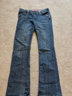  bootcut jeans   - Säljer ett par blå bootcut jeans från Esprit med snygga detaljer som dragkedja på bakfickan och dekorativt E-märke i midjan. Klassisk femficksmodell i bomull med normal passform och låg midja. Perfekta till sneakers eller boots.