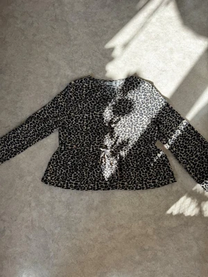Leopardmönstrad blus med knyt - Snygg leopardmönstrad blus med lång ärm och knyt i midjan. Blusen har rund halsringning och är tillverkad i ett mjukt, lätt tyg som ger en skön passform. Perfekt för dig som vill sticka ut med ett trendigt djurmönster.