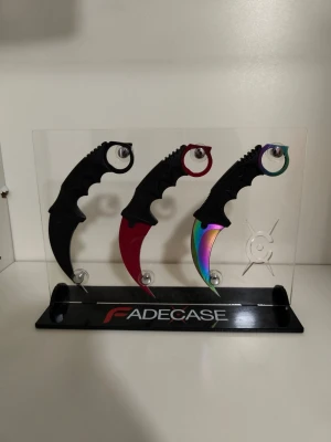 Karambitknivar med display från Fadecase - Säljer tre karambitknivar från Fadecase med en tillhörande snygg genomskinlig display. Knivarna har svarta handtag och bladen är svarta, röda och regnbågsfärgade. Perfekt för samlare eller som dekoration.