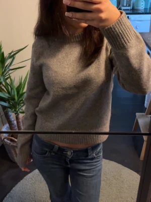 Grå stickad tröja från H&M - Mysig grå stickad tröja med rund halsringning och ribbade muddar vid ärmslut och nederkant. Perfekt för sommarkvällar och enkel att matcha med jeans eller kjol.
