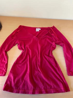 Röd långärmad topp med snörning - En röd långärmad topp med v-ringning. Toppen har en något utsvängd passform och är tillverkad i mjuk bomull, perfekt för en avslappnad och trendig look eller om man vill stylea den som the 2000s✨😉