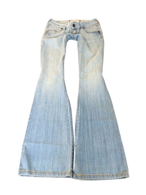 Ljusblå utsvängda jeans  - Säljer ett par ljusblå jeans från Joskicko med riktigt breda utsvängda ben och låg midja. Jeansen har klassiska fem fickor, slitna detaljer och knappgylf. Perfekta för dig som gillar retrostil och vill sticka ut med en cool siluett.